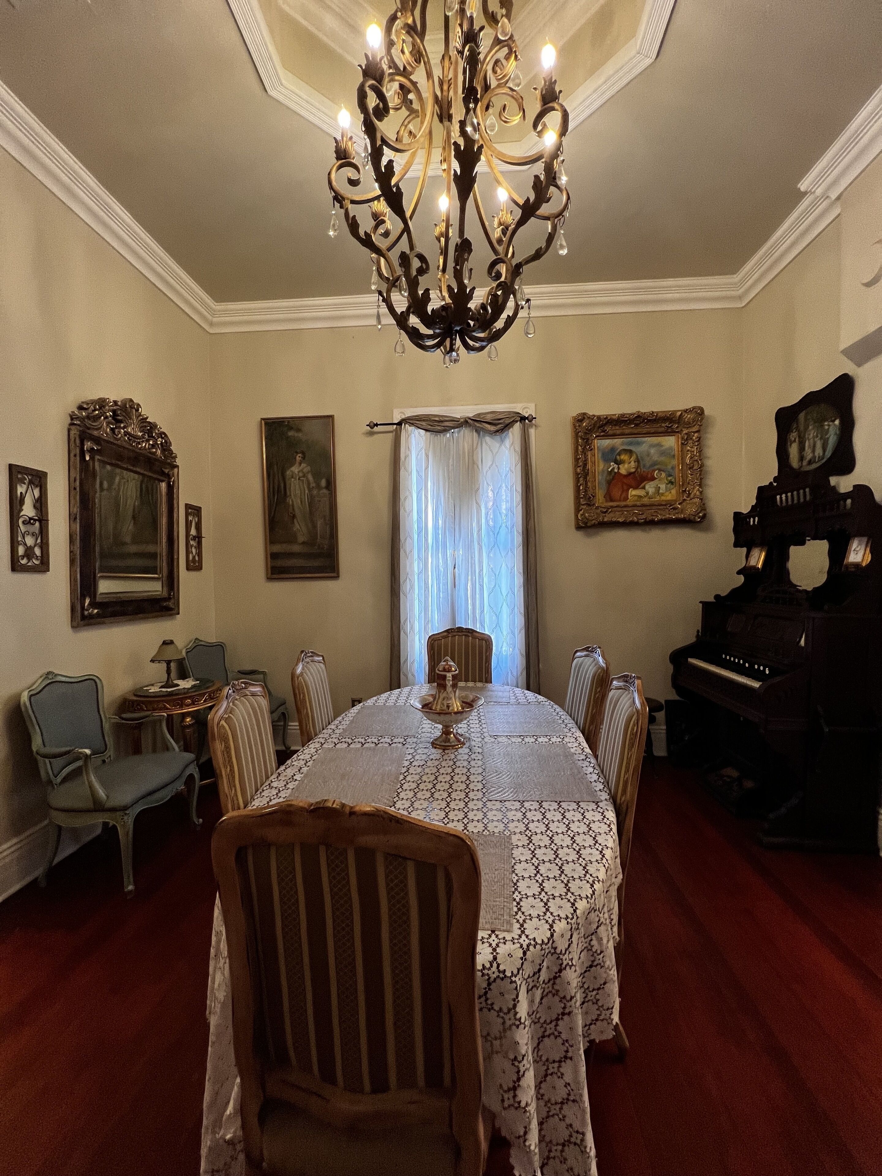 A formal dining room with a chandelier, a piano, and framed artwork on the walls.