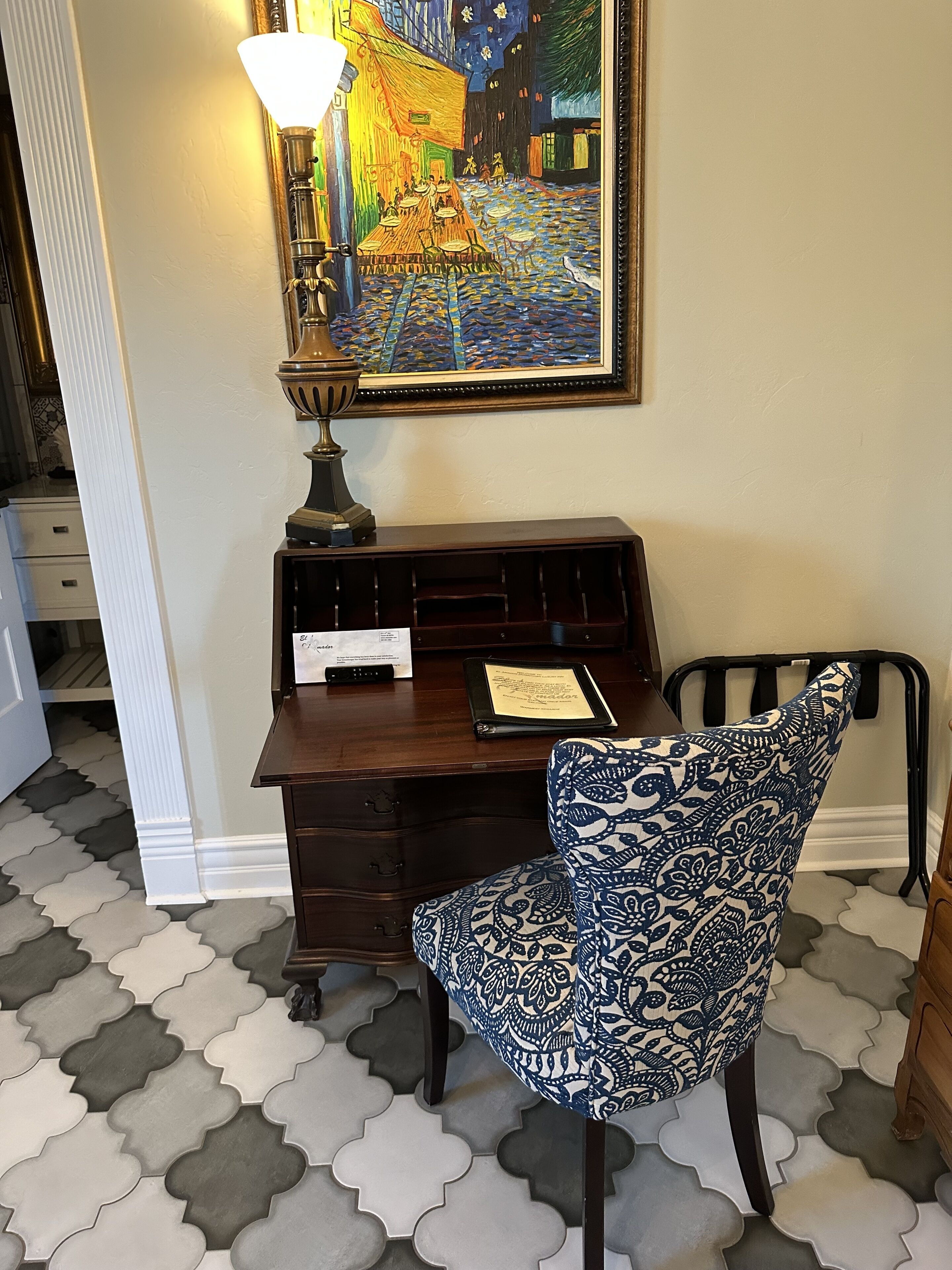 A study room with a desk, a chair, a lamp, and a framed painting on the wall.