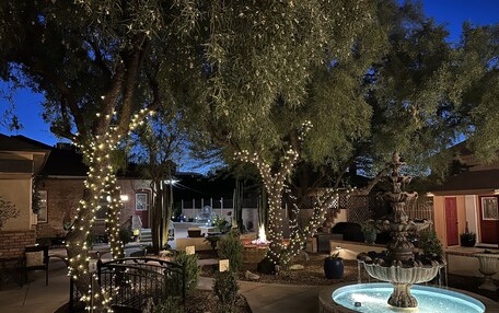 A courtyard with a fountain, trees wrapped in lights, and a brick building in the background.
