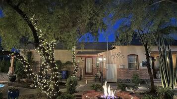 A patio area with a fire pit, outdoor seating, and a tree decorated with lights.