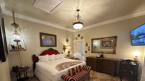 A spacious bedroom with a large bed, a vanity with a mirror, a television, and a chandelier. - El Amador Inn Downtown Tucson (Tucson)