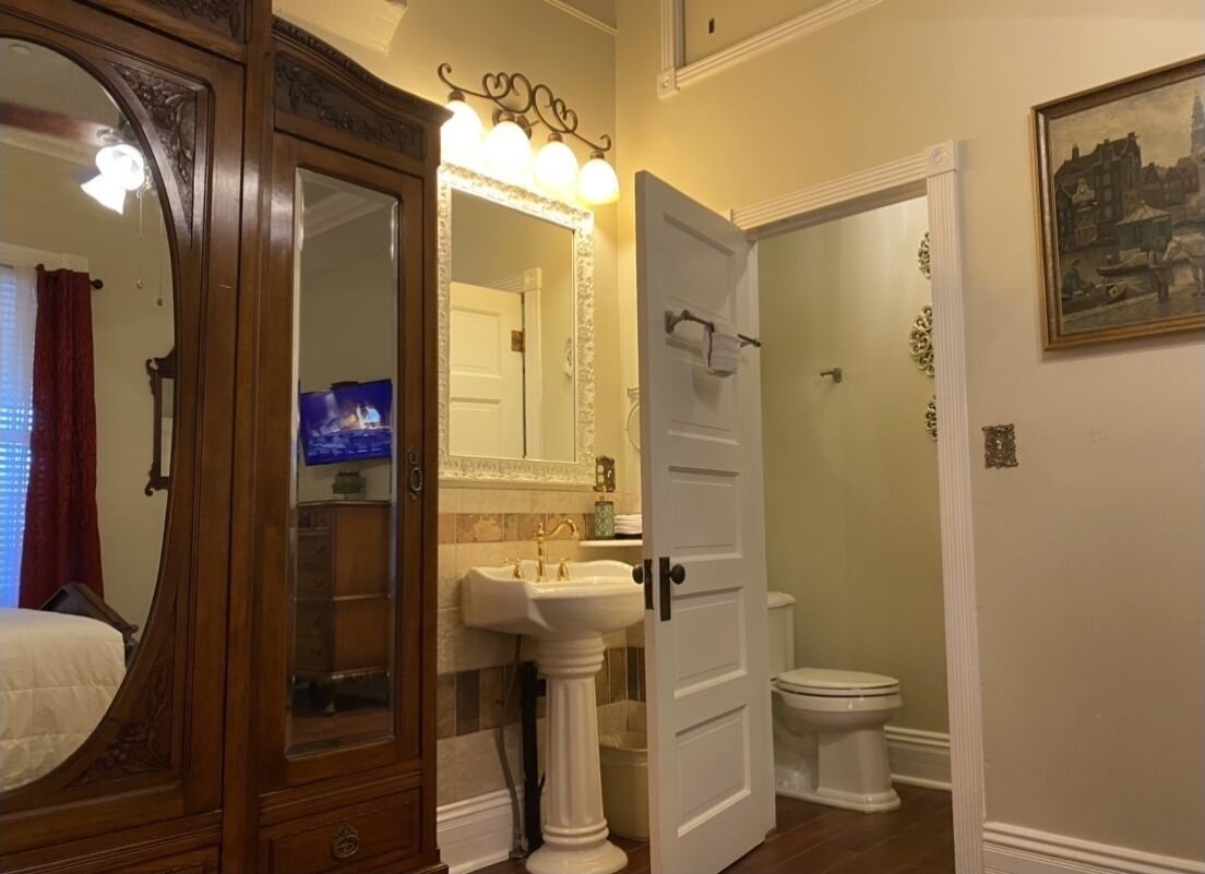 Ein Badezimmer mit einem Standwaschbecken, einem beleuchteten Spiegel, einer Toilette und einer Tür zu einem anderen Raum.