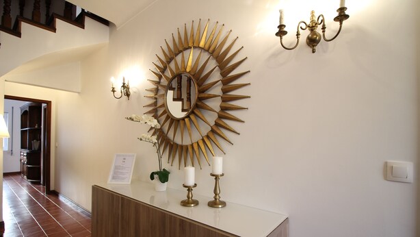 A reception area with a large mirror, a wooden cabinet, and a wall-mounted light fixture. - Comfortable house with magnificent garden (Ponta Delgada)