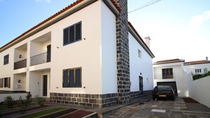 A two-story house with a white exterior, a red-tiled roof, and a brick chimney. There is a car parked in the driveway. - Comfortable house with magnificent garden (Ponta Delgada)