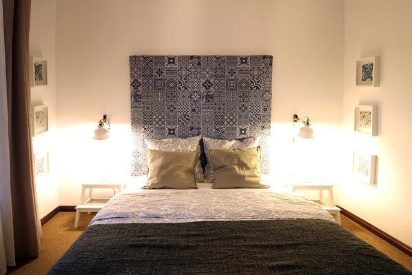 A neatly made bed with a patterned headboard, two bedside tables with lamps, and framed artwork on the walls.