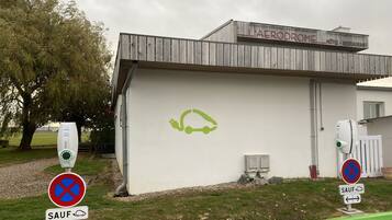 Een gebouw met een bord waarop 'L'AERODROME HOTEL RESTAURANT' staat en een groene oplaadstation voor elektrische auto's.