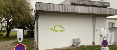 A building with a sign reading "L'AERODROME HOTEL RESTAURANT" and a green car charging station.