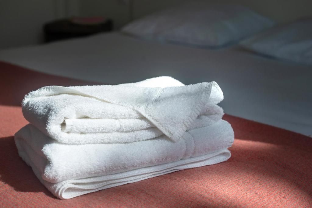 Un mucchio di asciugamani bianchi su un ripiano, con un letto sullo sfondo.