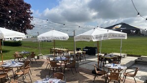 An outdoor dining area with tables and chairs, umbrellas, and a grassy field in the background. - l'Aérodrome de la Baie de Somme (Buigny-Saint-Maclou)