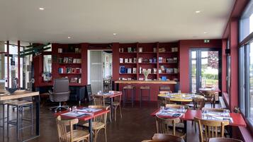 A library with bookshelves, tables, chairs, and a large window.