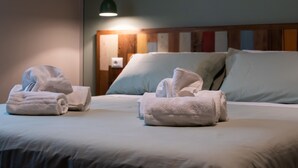A hotel room with neatly folded towels on the bed, a wooden headboard, and a green pendant light. - L' Eroico (Gaiole in Chianti)
