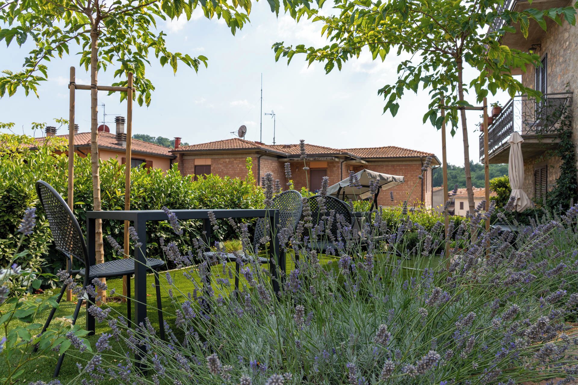 A garden with lavender plants, a metal fence, and a building with a tiled roof in the background.