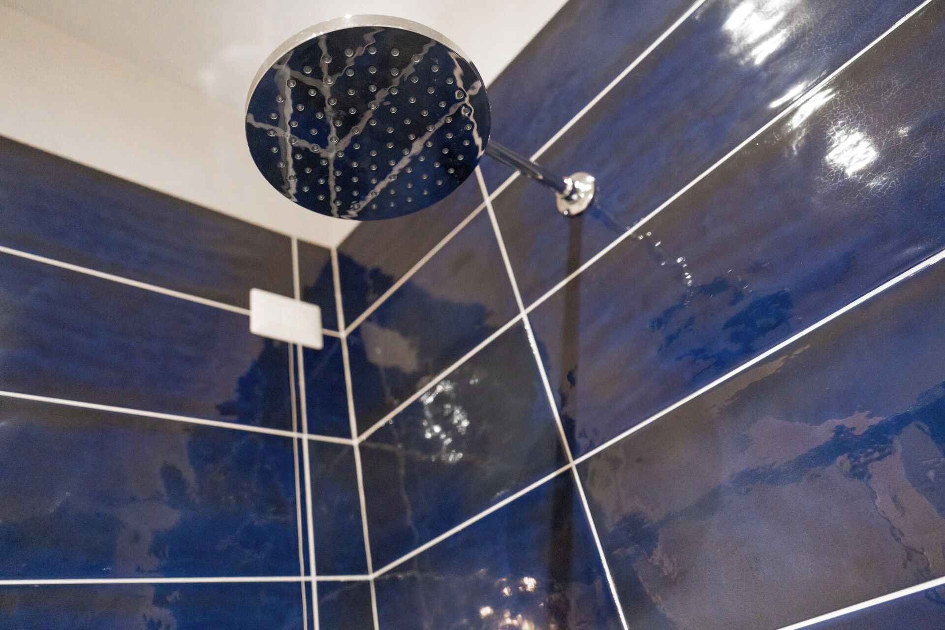 A modern bathroom with glossy blue tiles and a circular shower head.