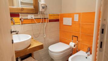 A bathroom with a sink, toilet, and bidet, a hairdryer, and a towel rack.