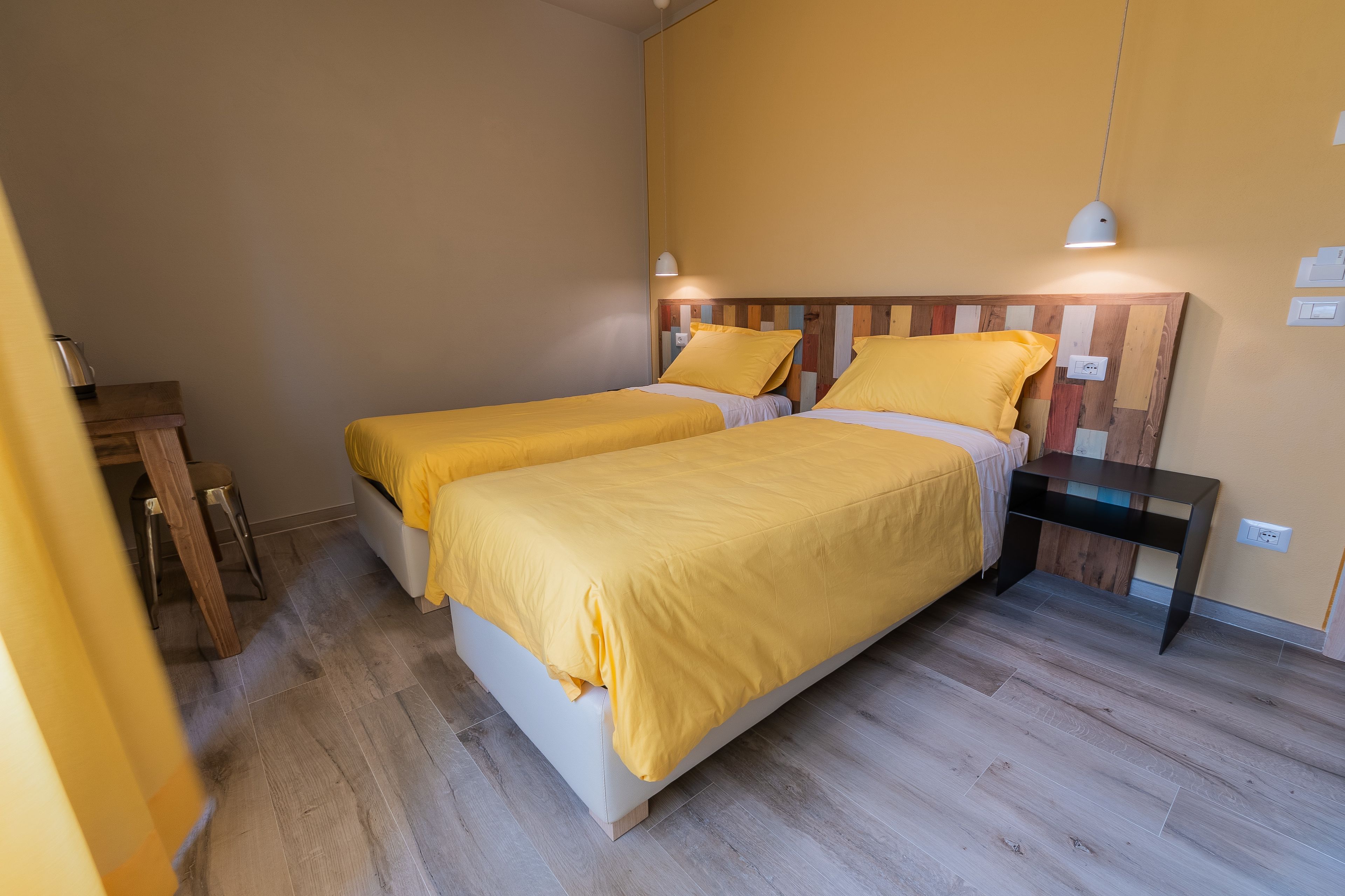 A room with two beds, wooden headboard, bedside tables, and a lamp.