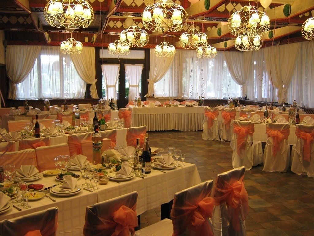 A banquet hall with round tables set for a formal event, featuring white tablecloths and orange sashes.