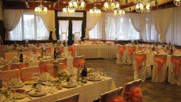 A banquet hall with round tables set for a formal event, featuring white tablecloths and orange sashes.