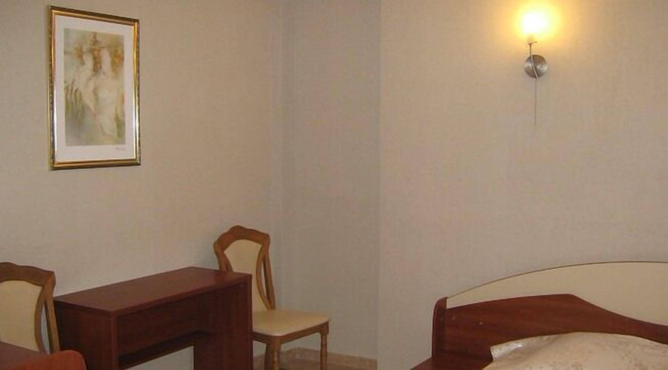 Una habitación con una cama, un escritorio y una silla. Hay un aplique de pared y un cuadro en la pared.