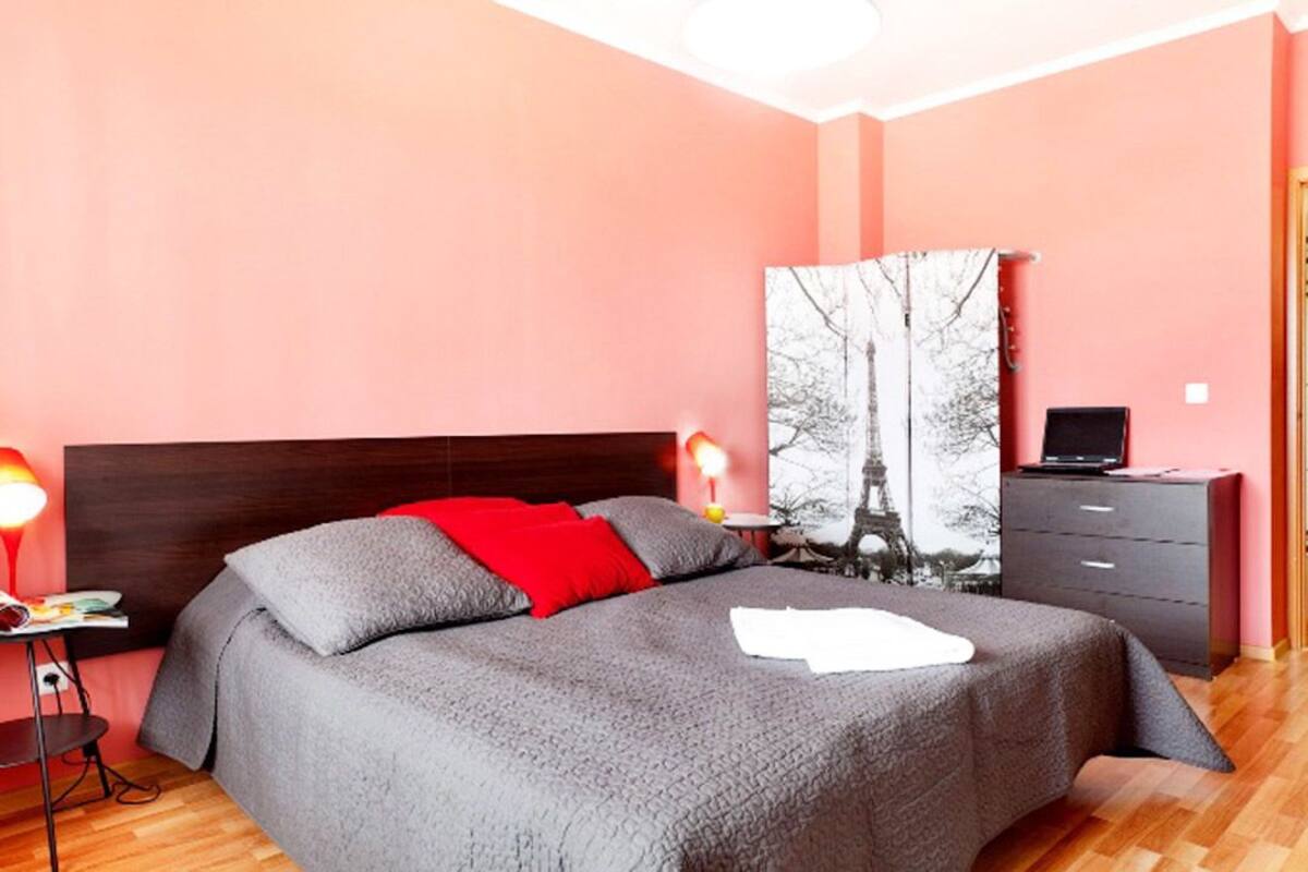 Ein Schlafzimmer mit Bett, Nachttisch, Lampe, Kommode und einem Gemälde an der Wand.