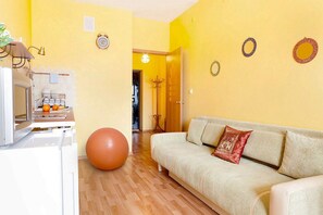 Olohuoneessa on sohva, suuri jumppapallo, keittiöalue jääkaapilla sekä ruokapöytä tuoleineen.