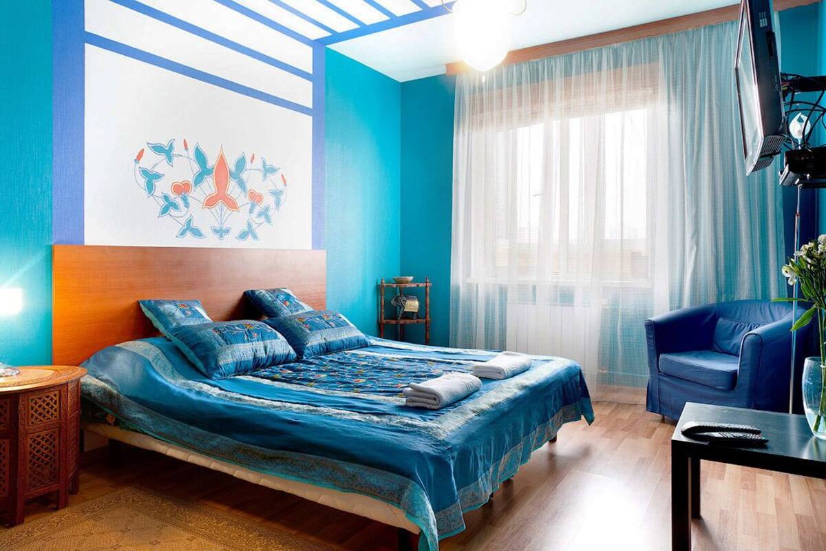 Ein Schlafzimmer mit einem Bett, einem blauen Sofa, einem kleinen Tisch und einem Fenster mit durchsichtigen Vorhängen.