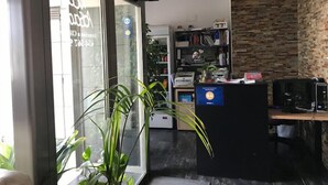 Un comptoir d’accueil avec un ordinateur, une plante et une bibliothèque en arrière-plan.