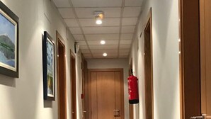 Un couloir avec des portes en bois, des tableaux encadrés accrochés aux murs, un extincteur et un sol carrelé.