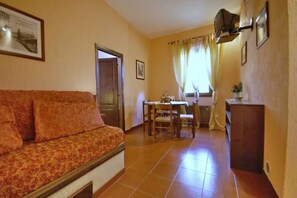 A living room with a sofa, a dining table with chairs, a small kitchen area, and a door leading to another room. - Apt. LaTraviata - Residence Casa lama - two-room apartment 2/4 P for couples or families (Castelfranco di Sopra)