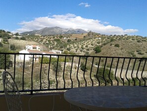 Un balcone con vista su un paesaggio montuoso, che include case e un cielo sereno.