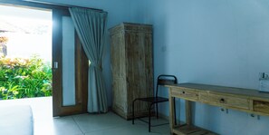 A room with a wooden desk, a chair, a wardrobe, and a sliding glass door leading to a garden. - The Wina Guesthouse 2 (Canggu)