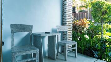 A patio area with two wooden chairs and a small table, surrounded by a brick wall and lush greenery.