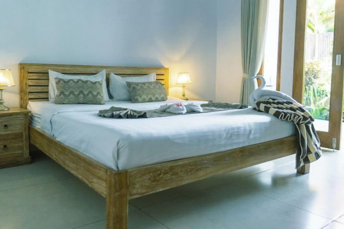 A bedroom with a wooden bed, two bedside tables with lamps, and a view of the outdoors.