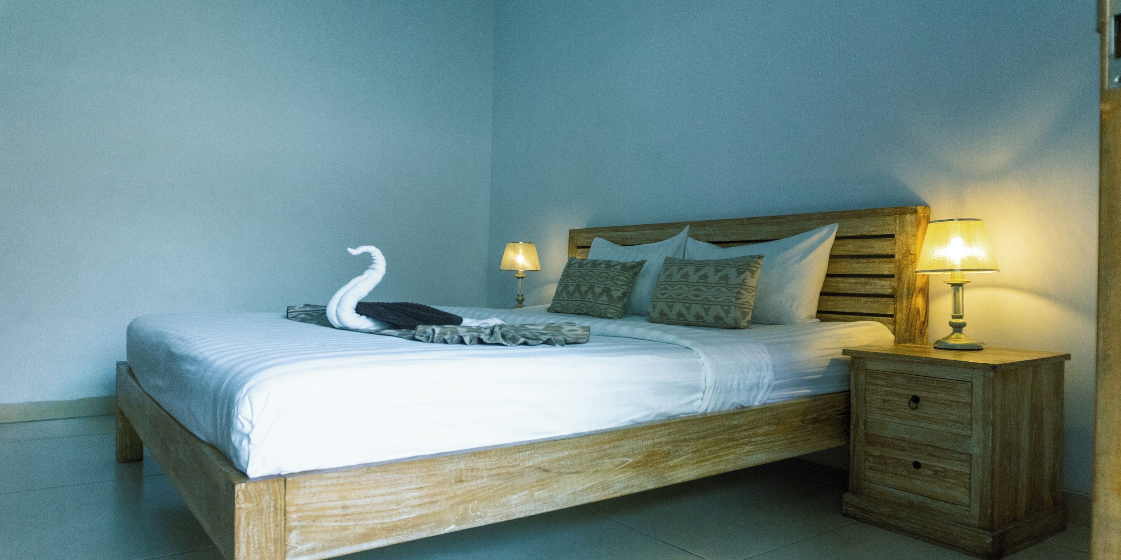 A single bed with a wooden frame, two bedside lamps, and a swan decoration on the bed.