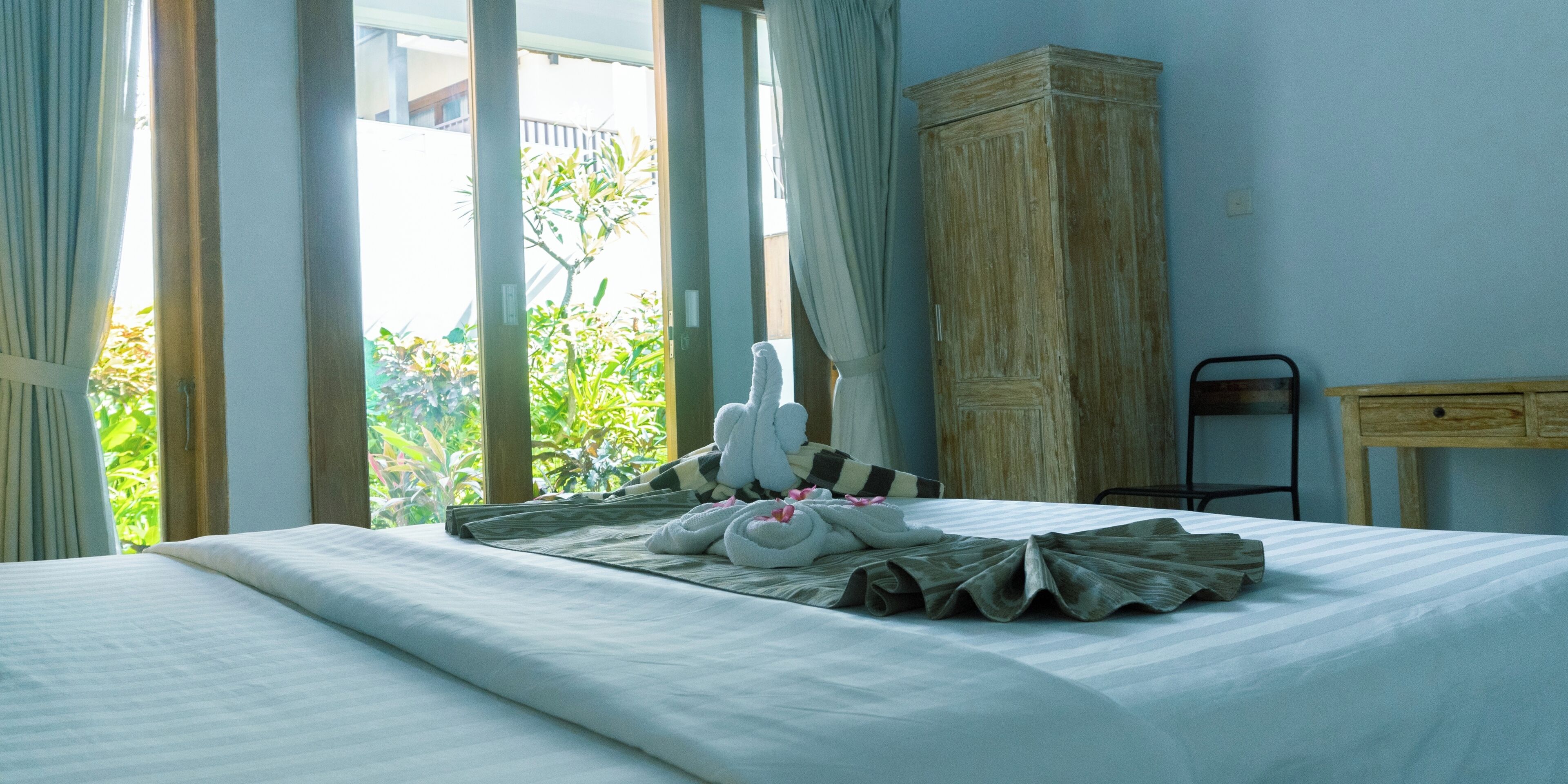 A hotel room with a bed, a wooden wardrobe, and a view of greenery outside.