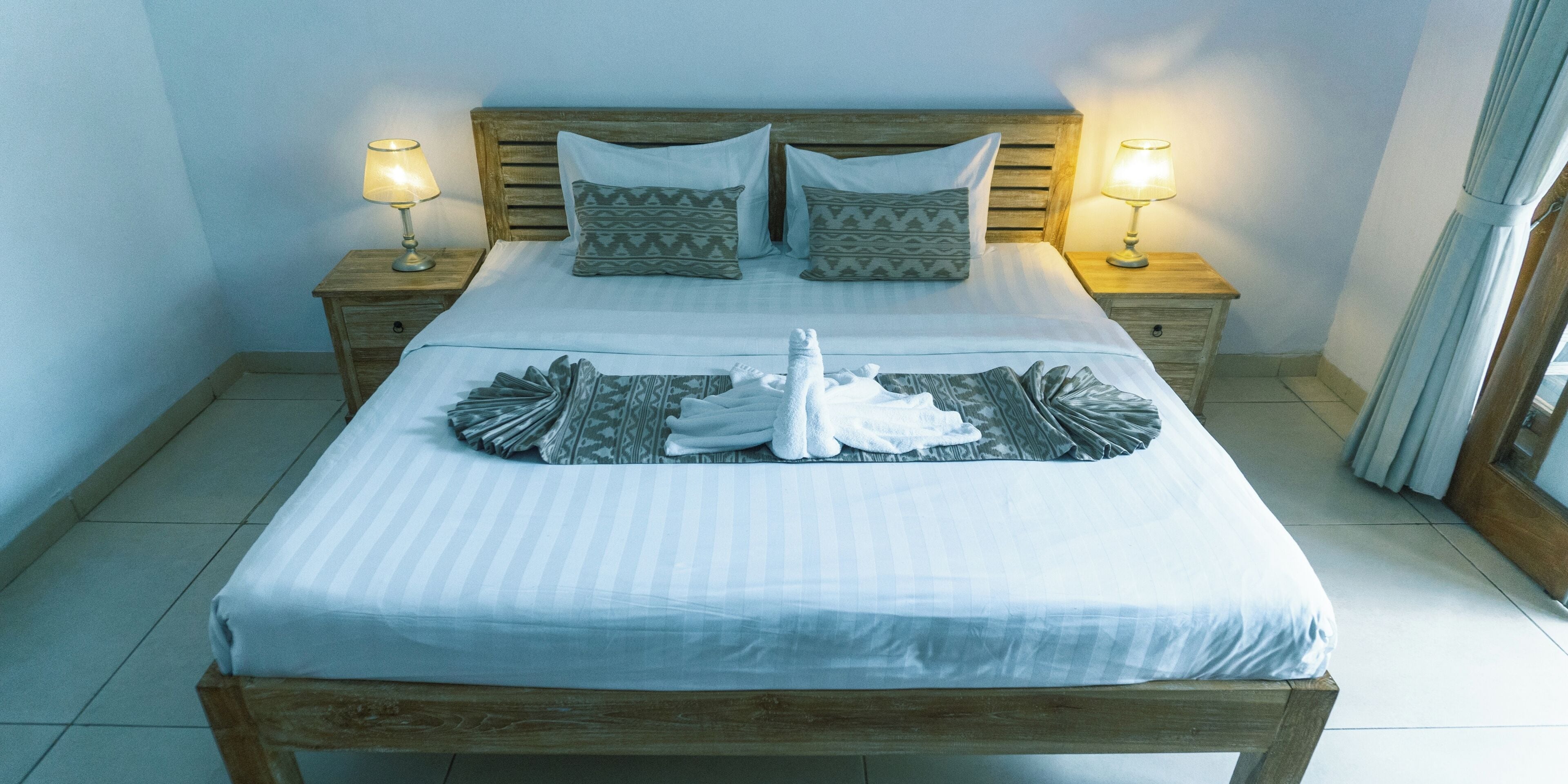 A neatly made bed with two pillows, two bedside lamps, and a folded towel on the bed.