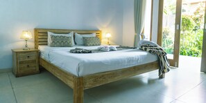 A wooden bed with white linens, two bedside lamps, and a view of greenery outside. - The Wina Guesthouse 2 (Canggu)