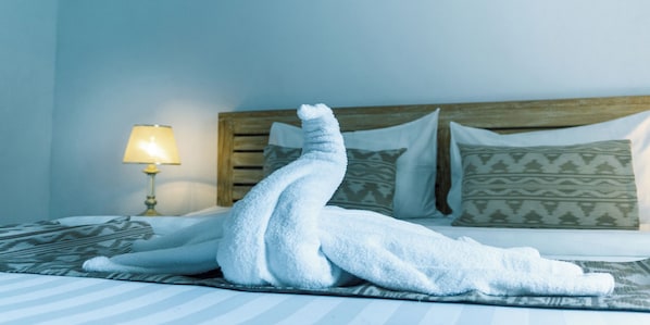 A bed with a white towel arranged in a swan shape, a patterned pillow, and a bedside lamp.
