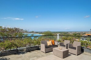 A balcony with wicker furniture and a view of the beach and cityscape.