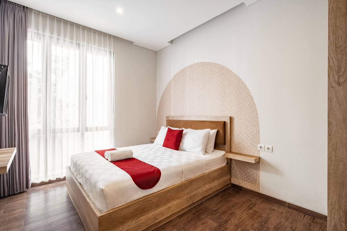 Una habitación de hotel moderna con una cama de madera, ropa de cama blanca y un plaid rojo.