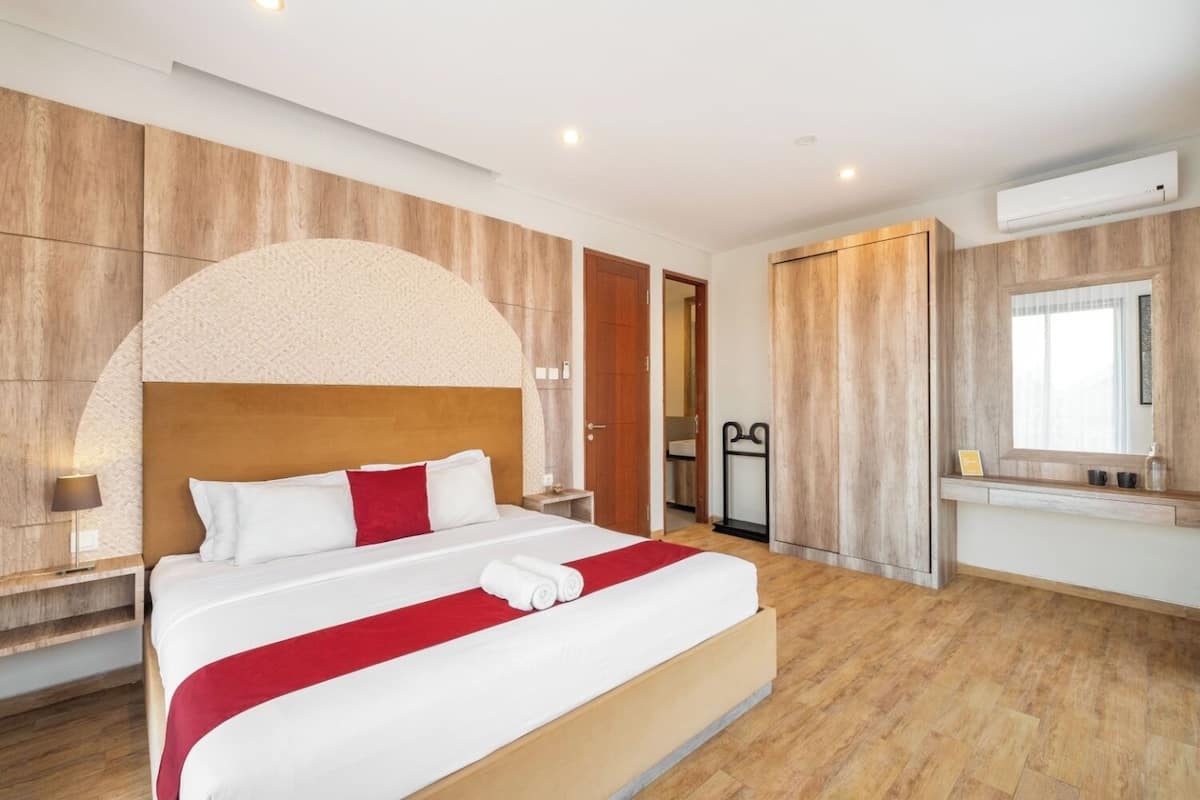 Una habitación de hotel moderna con una cama grande, paneles de madera, un armario empotrado y un baño visible a través de una puerta abierta.