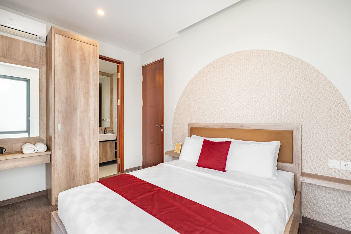 Una habitación de hotel moderna con una cama, un armario de madera, un baño y un ventanal grande en arco.