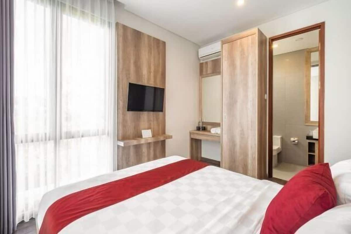 Habitación de hotel con cama, televisor montado en la pared, baño visible a través de una puerta abierta y un espejo grande.