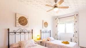 Un dormitorio con dos camas, un ventilador de techo y una ventana con cortinas florales.