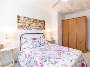 Een slaapkamer met een bloemenbedekker, een houten kledingkast en een plafond met een bladmotief.