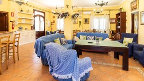 Amplia sala de estar con sofá, sillones y comedor. Cuenta con múltiples lámparas colgantes y una chimenea.