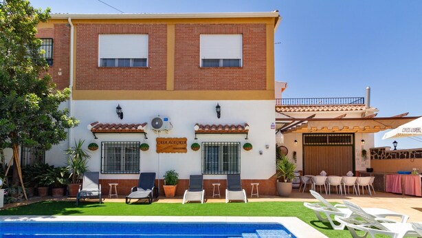 Un edificio de dos pisos con piscina, mobiliario exterior y plantas en macetas.