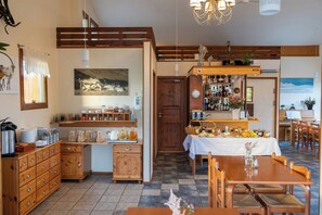 A cozy dining area with a wooden table and chairs, a buffet table with various food items, and a bar area with bottles and glasses. - Arnanes Country Hotel (Höfn)