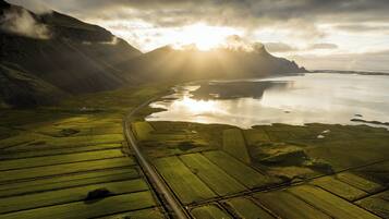 An aerial view of a coastal landscape with fields, a road, and mountains.