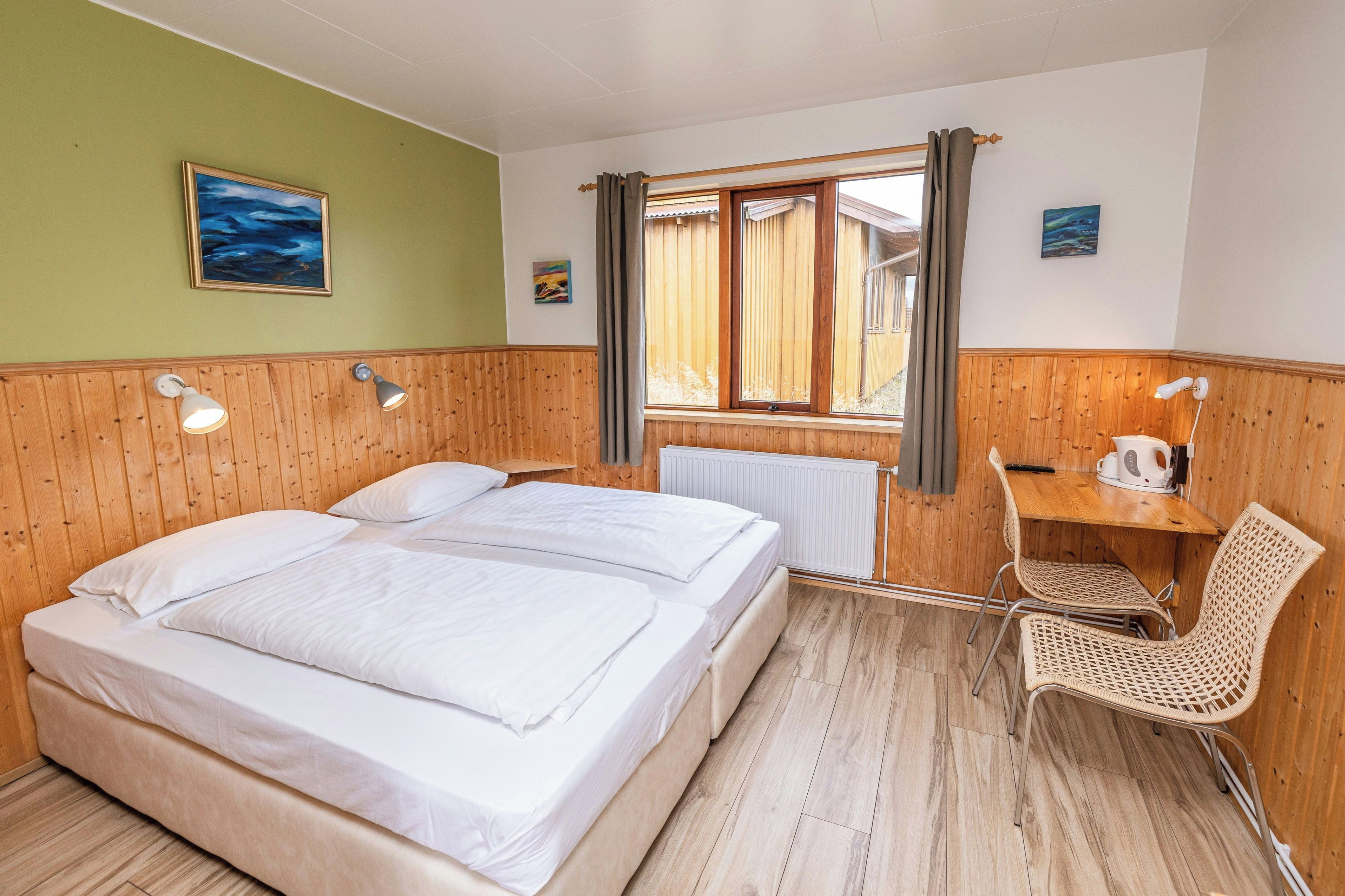 Une chambre d’hôtel avec deux lits, un bureau, une chaise, un radiateur et une fenêtre avec des rideaux.