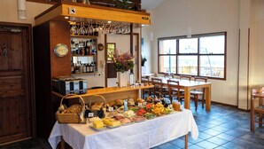A breakfast buffet with various food items, a bar area with shelves of bottles, and a dining area with wooden furniture. - Arnanes Country Hotel (Höfn)